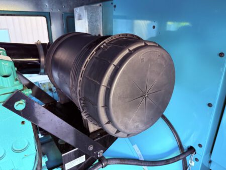 Close-up of the Cummins generator’s cylindrical air cleaner housing mounted on the engine, showing intake filter cover and locking mechanism.
