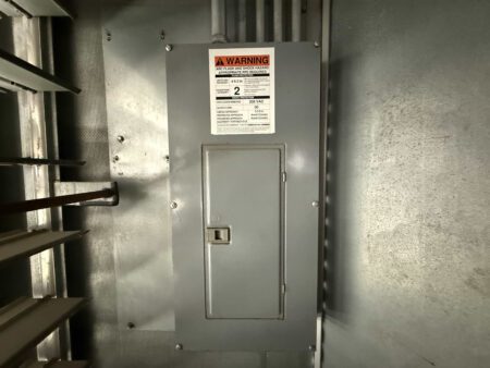Closed breaker panel with safety warning label inside Caterpillar 3516C generator enclosure.