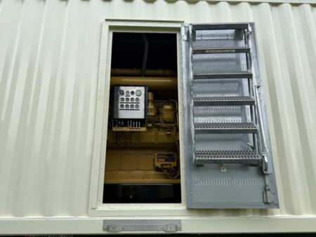 This image shows the breaker access door of a Caterpillar 3516C containerized generator enclosure in the open position. The exterior of the enclosure features ventilation louvers for cooling airflow, while the hinged door includes an integrated fold-out ladder step system for safe operator entry. Through the access opening, the generator circuit breaker and control distribution panels are clearly visible inside, providing convenient access for monitoring, maintenance, and electrical connection operations. This design ensures secure, weather-protected housing while maintaining operator safety and serviceability.