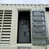 Side view of Caterpillar 3516C containerized generator enclosure showing breaker access door open with ladder steps and control panels visible inside.