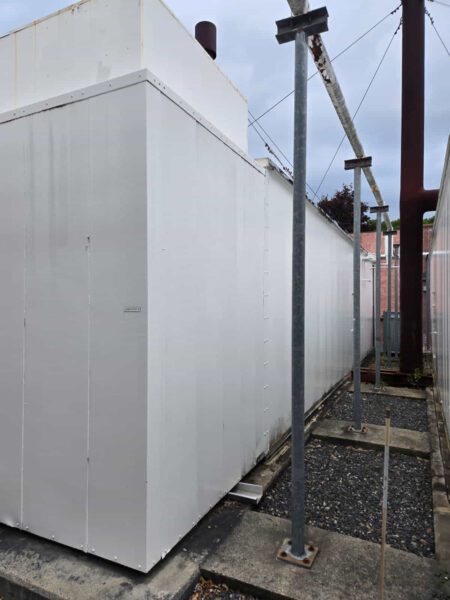 Angled side view of Caterpillar generator enclosure with white painted panels and exhaust system.